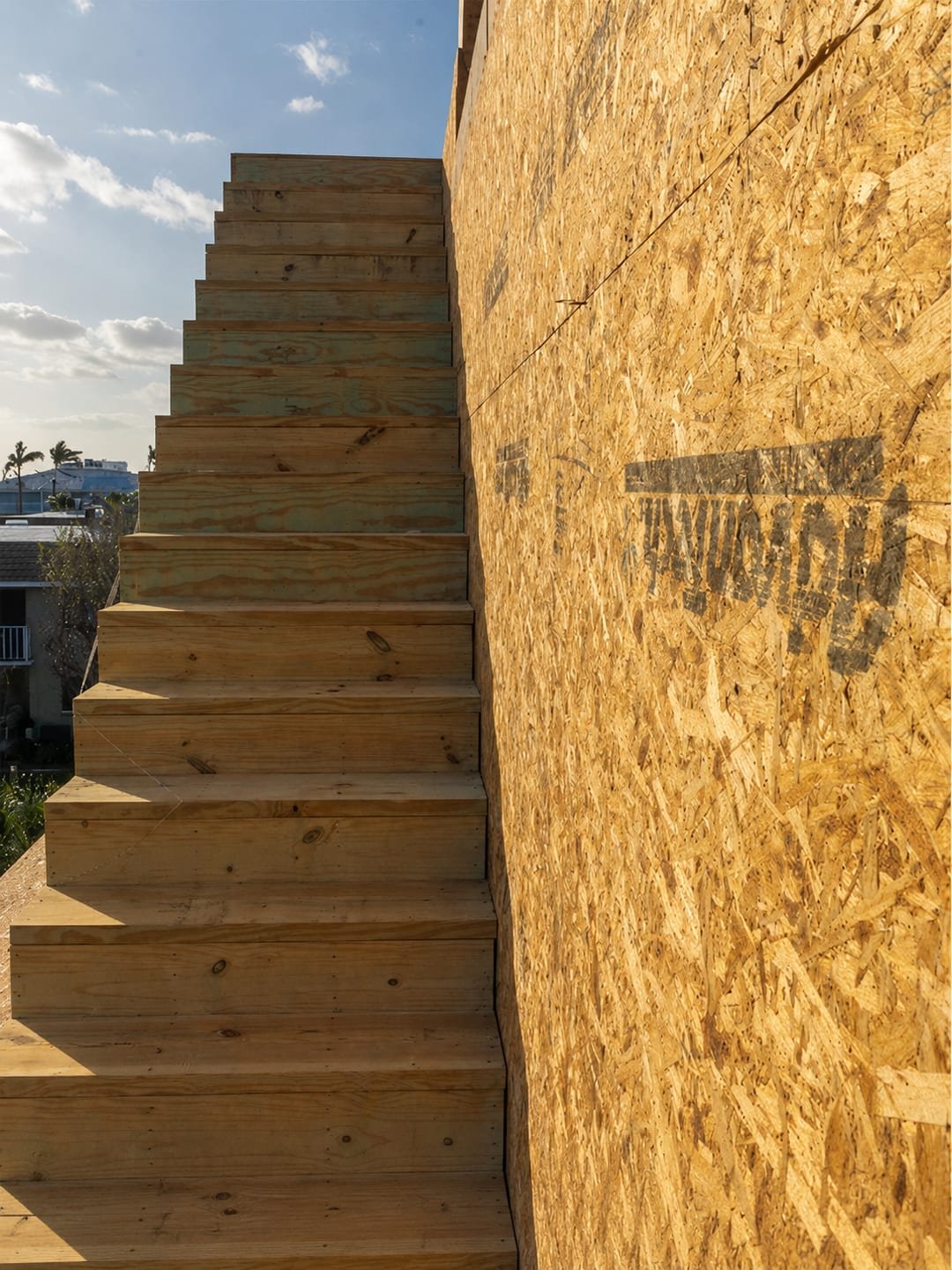 Second-story addition by Acosta Builders — framed exterior stair stringers and treads climbing a sheathed wall to the new upper level