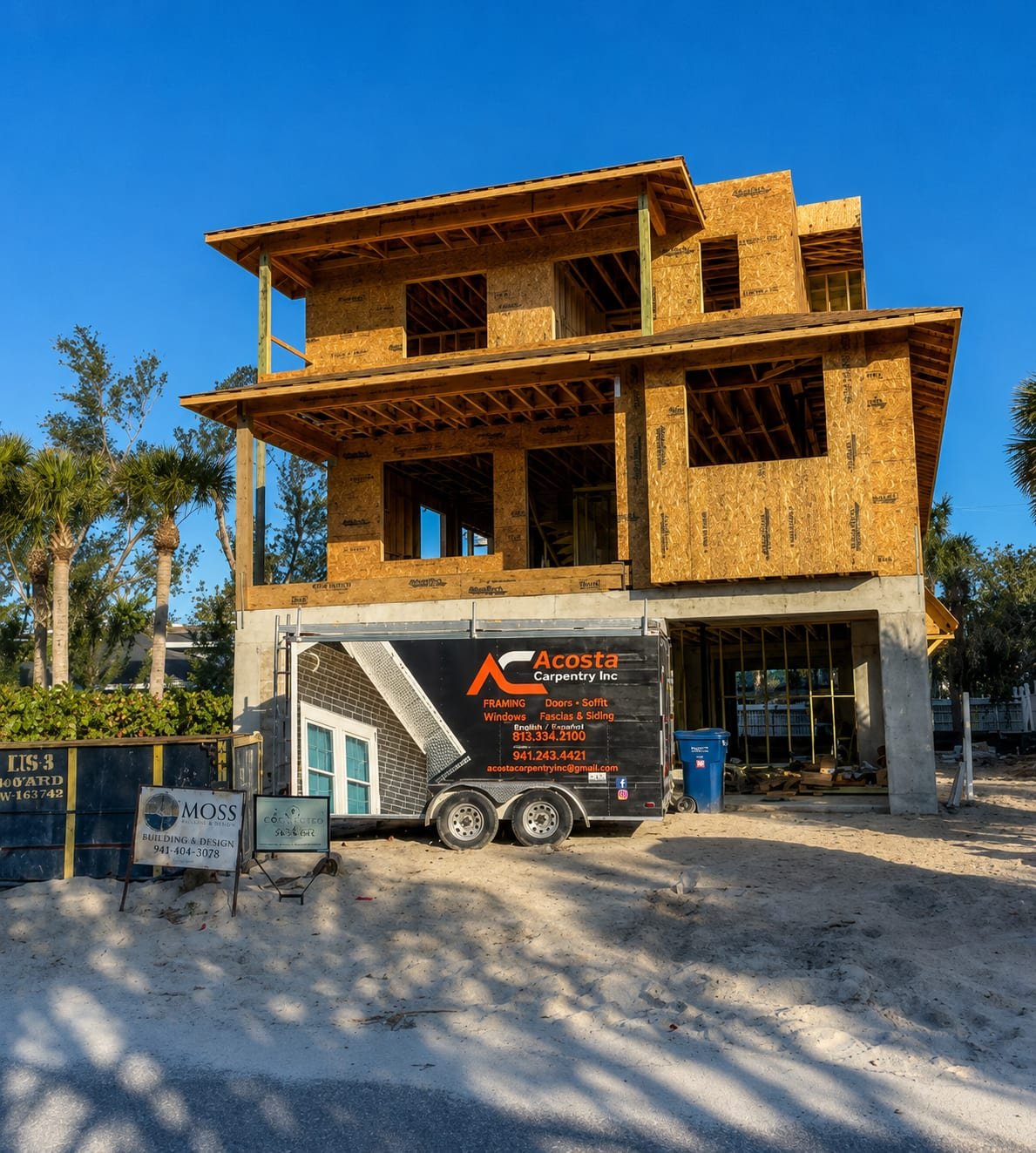 Three-storey elevated coastal home during framing by Acosta Builders — sheathed walls, stacked overhangs, and a piling foundation