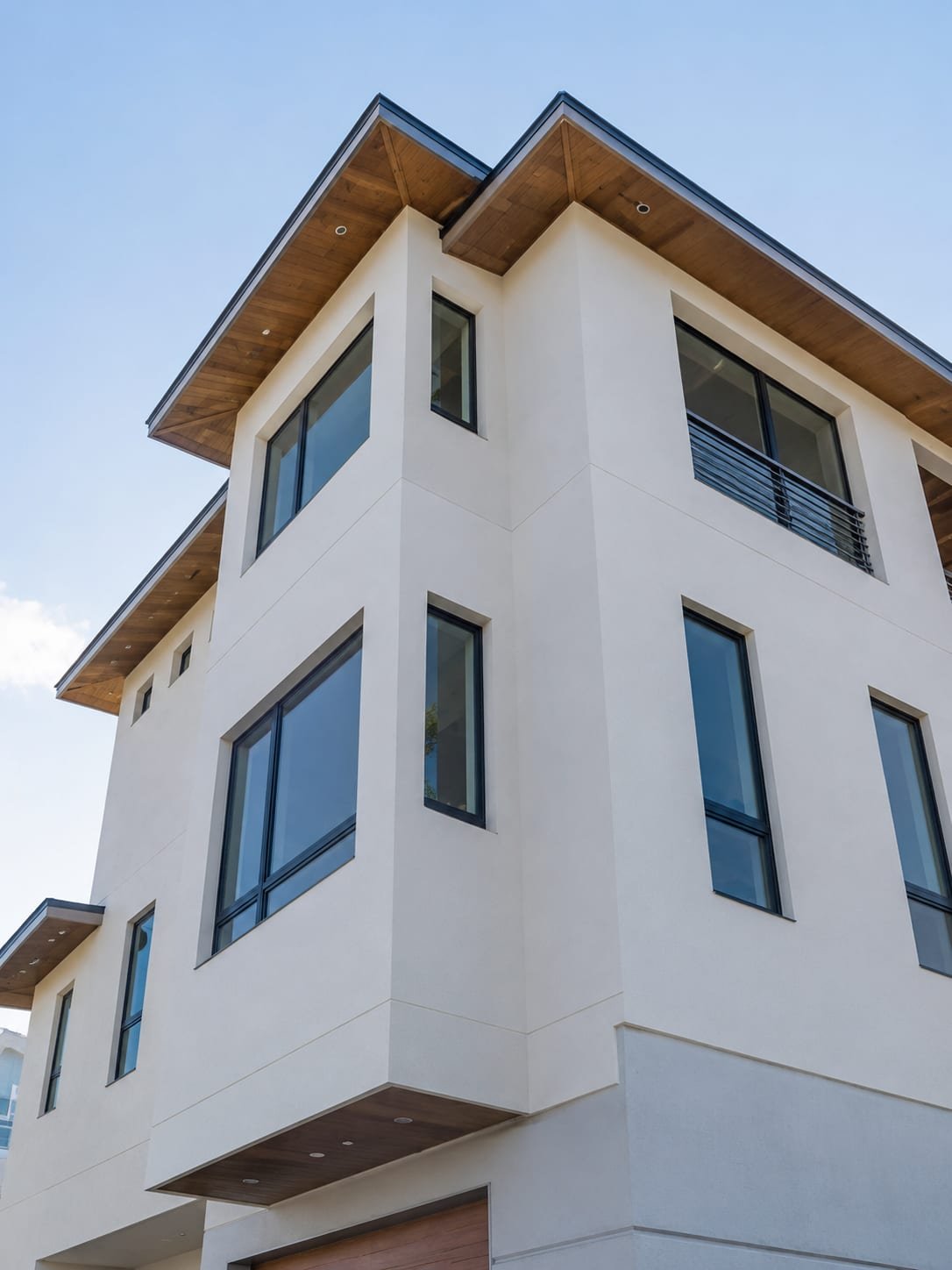 The same corner finished by Acosta Builders — smooth exterior, wood-clad soffit under deep eaves, and black-framed windows set into the openings