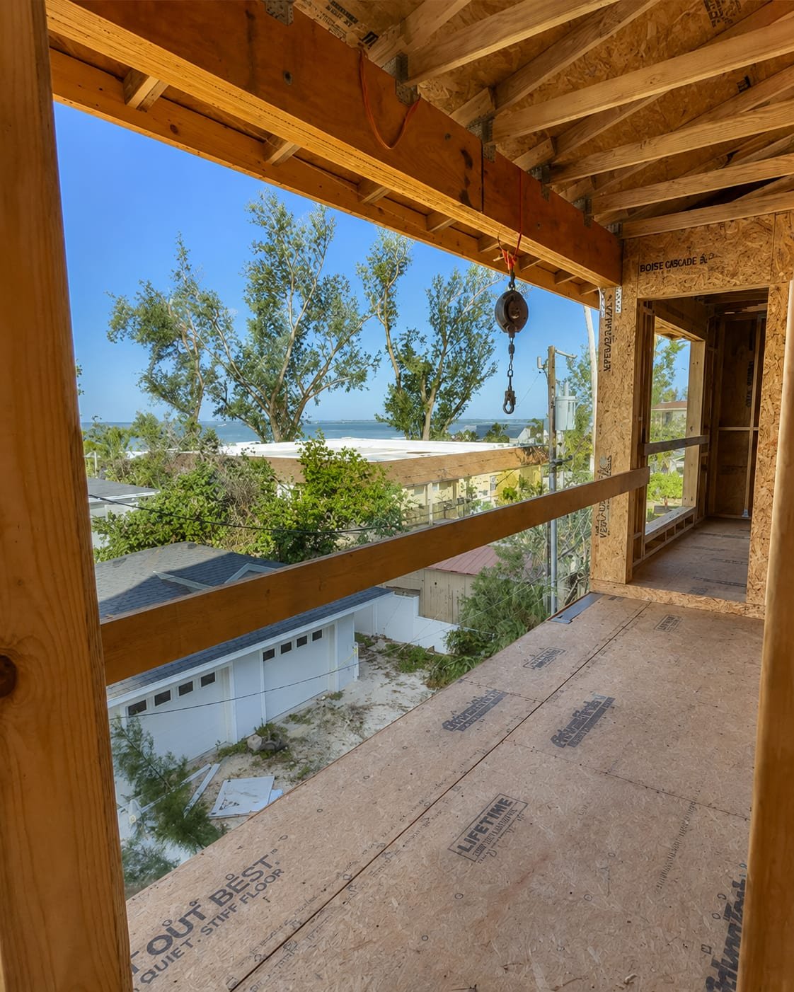 Framed second-floor opening by Acosta Builders — header beam, floor joists and subfloor sheathing with the Gulf visible beyond