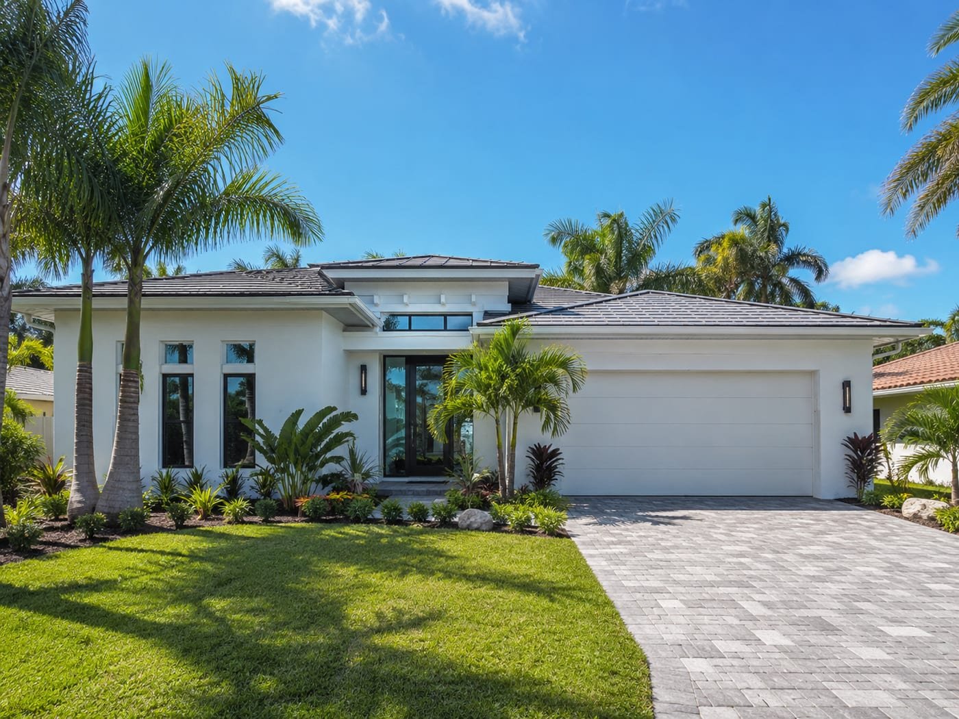 New home built by Acosta Builders in Bradenton, FL — coastal residence with white stucco, low-pitch tile roof, black-framed impact windows, and a paver driveway