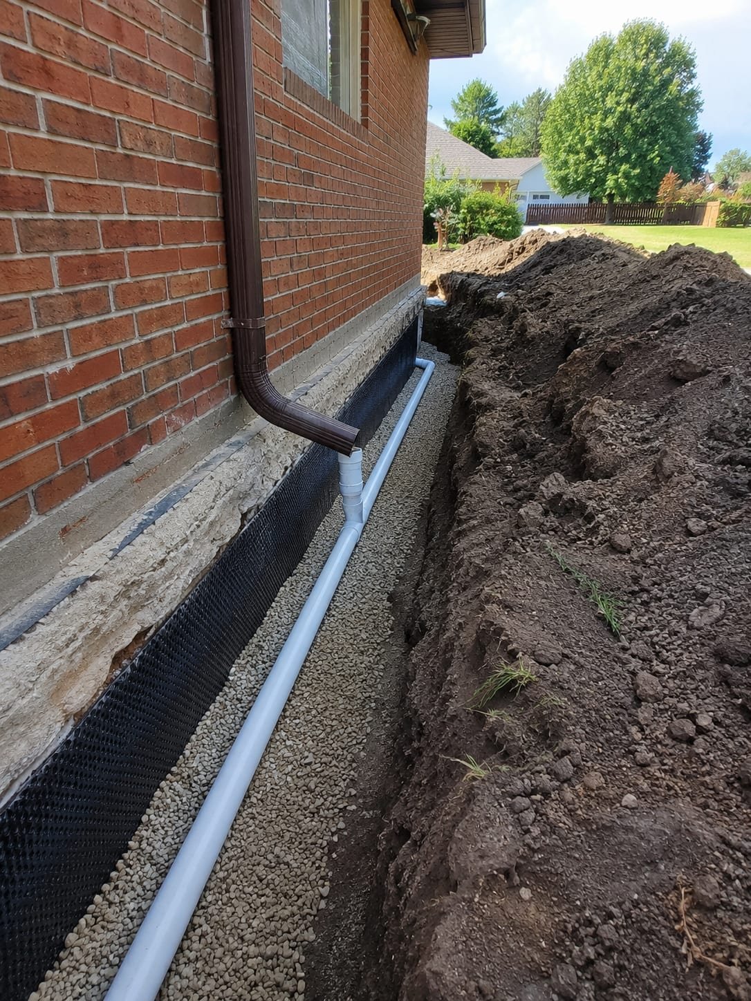 Foundation drainage and waterproofing by Acosta Builders — excavated footing with dimple membrane, gravel bed, and perimeter drain